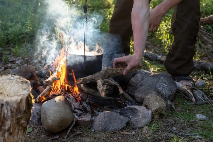 Man puts firewood on a campfire, on which he cooks food, in the camp. Tourism and active lifestyle.